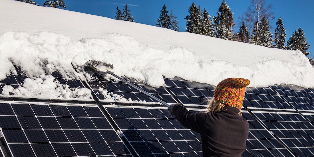 kvinna borstar bort snö från solpaneler på vintern